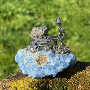 Figurine de mineur poussant une brouette de pyrite dorée sur un bloc de cristal de calcite bleue naturelle.