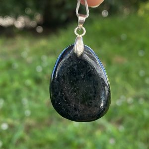 Pendentif en nuumite véritable du Groenland, en forme de goutte polie, monté sur une bélière. La pierre noire laisse apparaître des reflets irisés dorés et cuivrés.