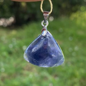 Gros plan d'un pendentif en tanzanite véritable de forme triangle, révélant de jolie reflets bleu et violet profond, monté sur une bélière en acier inoxydable.