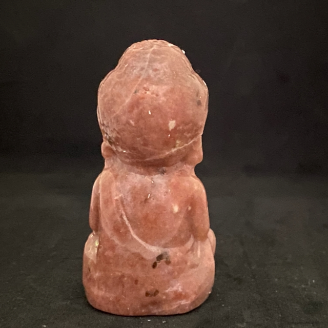 Vue de dos d'un petit bouddha en pierre rhodonite rose saumon, figurine sculptée en position de méditation.