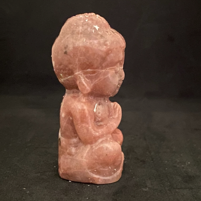 Profil d'un petit bouddha en pierre rhodonite rose saumon, figurine sculptée en position de méditation.